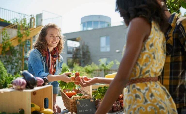 Woman selling organic vegetables to another woman at a market, highlighting plant-based lifestyle and sustainable choices.
