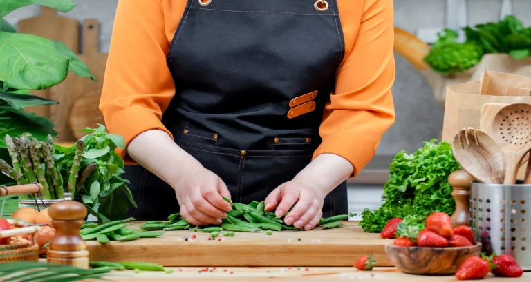Person preparing fresh vegetables on a cutting board at a table, promoting homegrown high-protein crops and healthy eating.